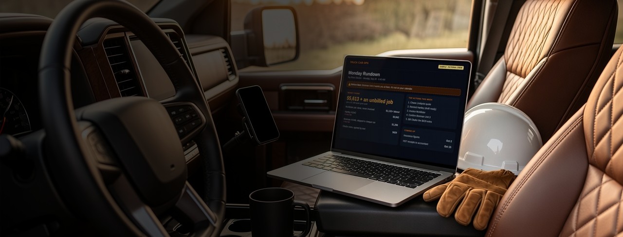A laptop showing the Monday Rundown on the console of a pickup truck, next to a hard hat and work gloves